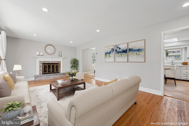 living area with recessed lighting, light wood finished floors, a glass covered fireplace, and baseboards