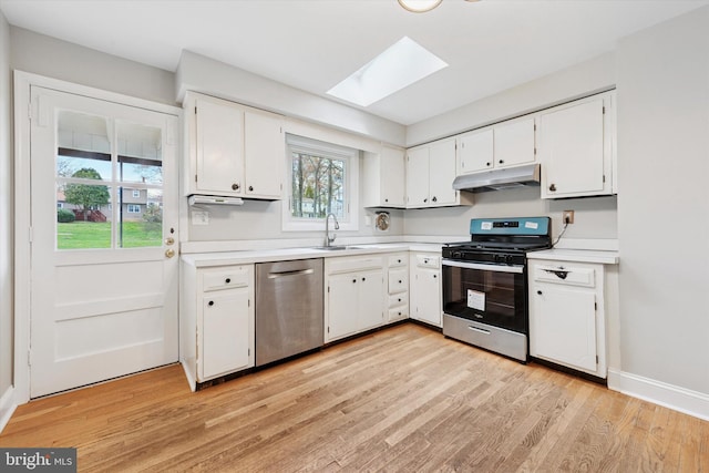 kitchen with appliances with stainless steel finishes, a sink, light wood finished floors, under cabinet range hood, and a skylight