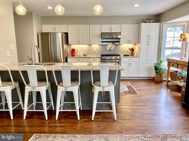 kitchen with under cabinet range hood, white cabinets, a sink, appliances with stainless steel finishes, and hanging light fixtures