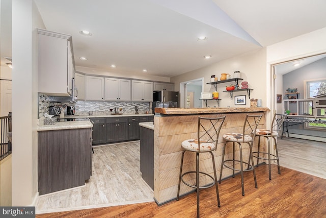 kitchen with a peninsula, light wood finished floors, freestanding refrigerator, and a breakfast bar area