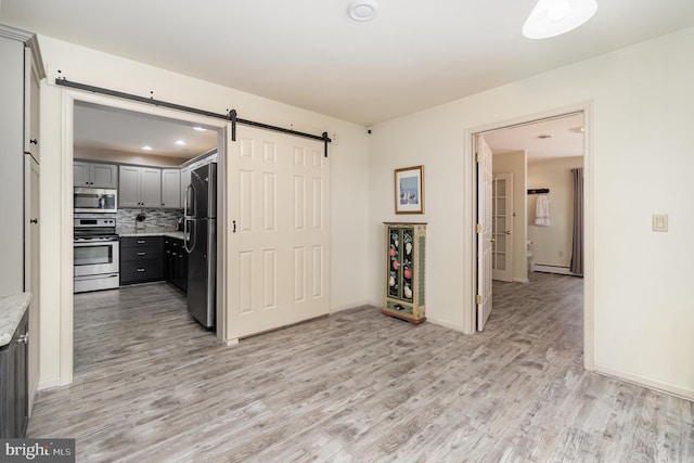kitchen with a barn door, light wood-style flooring, stainless steel appliances, decorative backsplash, and gray cabinetry