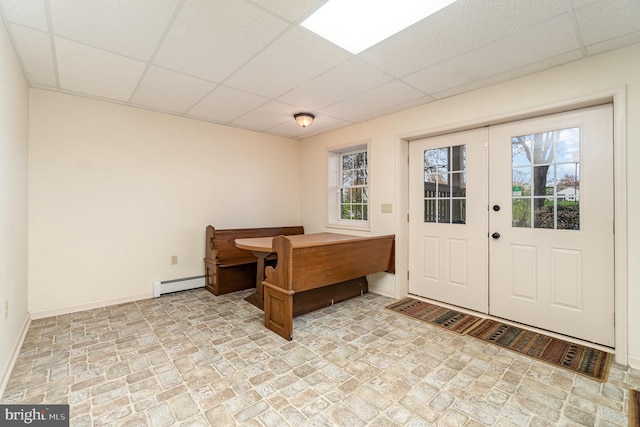 office space featuring baseboards, stone finish flooring, a drop ceiling, and a baseboard radiator