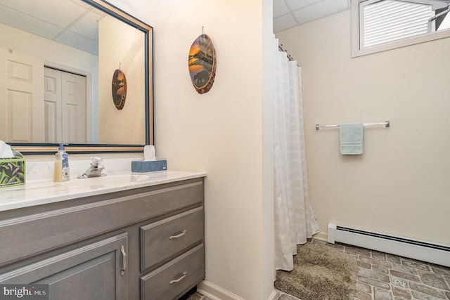 bathroom featuring baseboards, a baseboard heating unit, a drop ceiling, and vanity