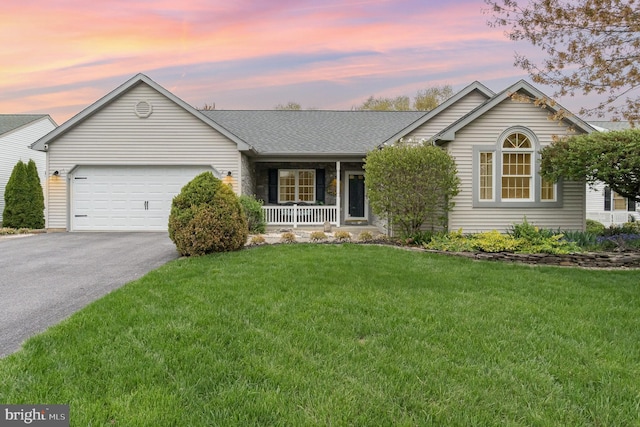 ranch-style home with aphalt driveway, covered porch, a shingled roof, an attached garage, and a yard