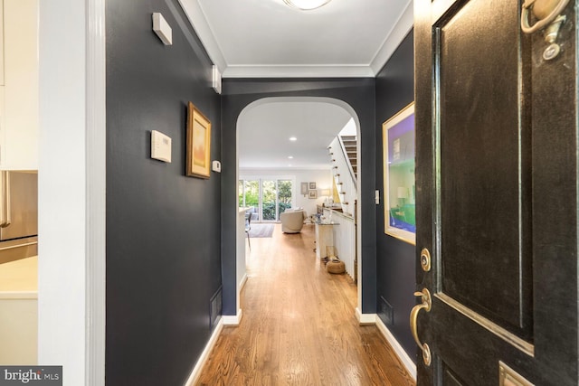hall featuring crown molding, arched walkways, baseboards, and wood finished floors