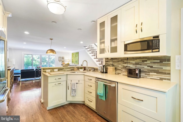 kitchen with appliances with stainless steel finishes, a sink, light countertops, dark wood finished floors, and a peninsula