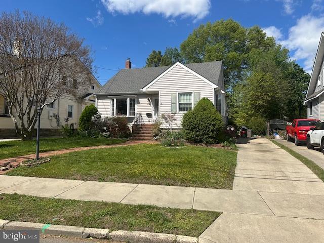 bungalow-style house featuring driveway, a chimney, and a front yard