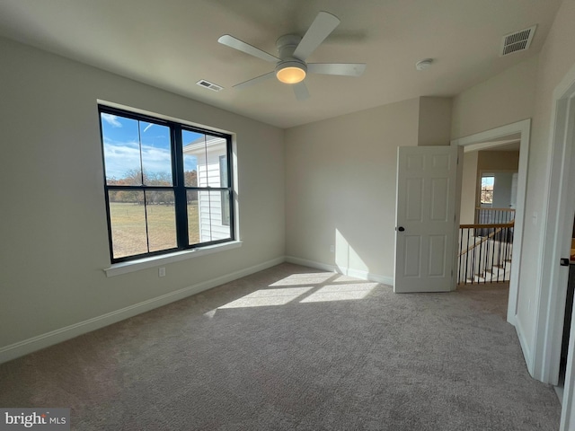 carpeted spare room with a ceiling fan, visible vents, and plenty of natural light