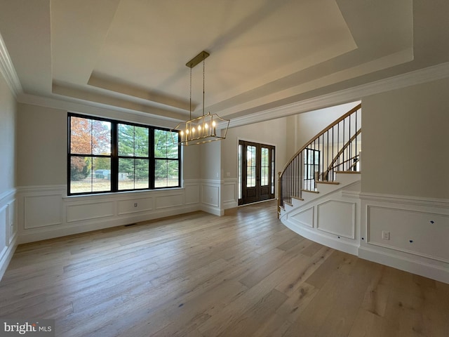 unfurnished dining area featuring light wood-style floors, a decorative wall, a tray ceiling, and a chandelier