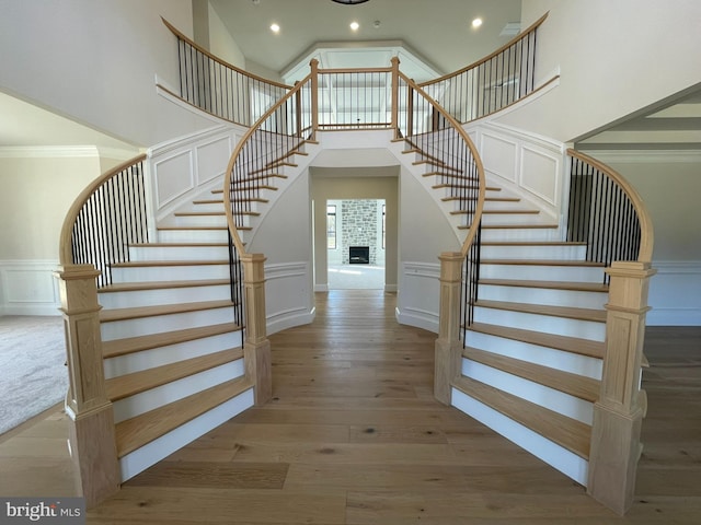 stairs featuring wainscoting, a decorative wall, a fireplace with raised hearth, recessed lighting, and wood finished floors
