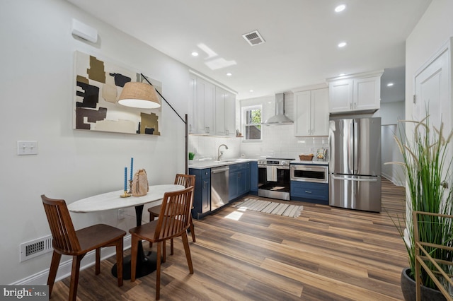 1544 N Allison St, Philadelphia, PA 19131 - kitchen featuring wall chimney range hood, blue cabinets, visible vents, white cabinets, and stainless steel appliances