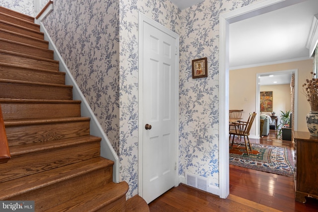 staircase featuring wood-type flooring, wallpapered walls, baseboards, and crown molding