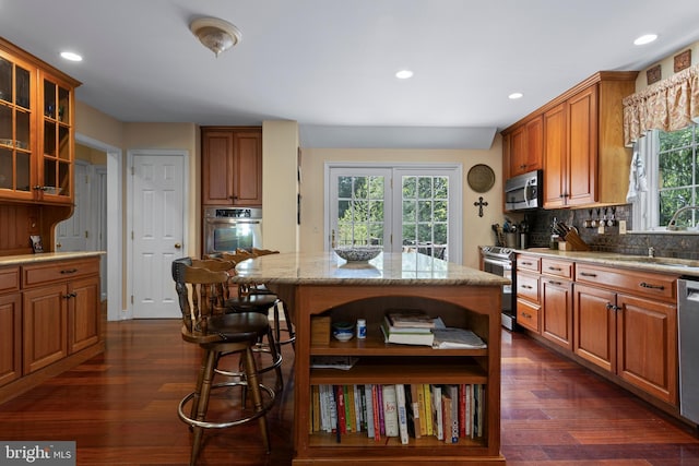 kitchen featuring stainless steel appliances, a sink, light stone countertops, brown cabinetry, and decorative backsplash