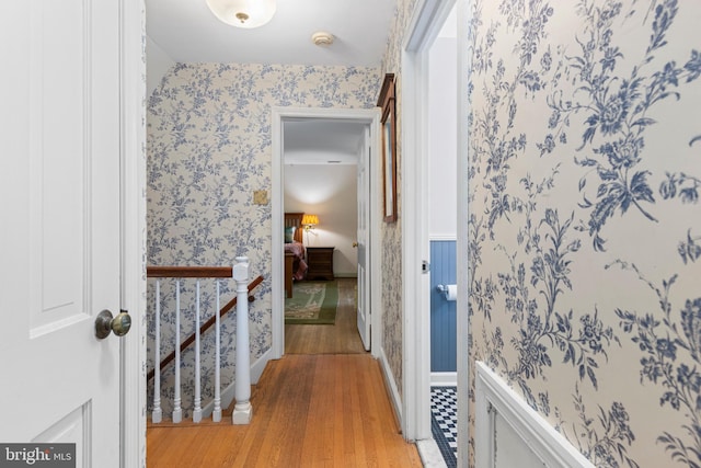 corridor with wallpapered walls, an upstairs landing, light wood-style flooring, and baseboards