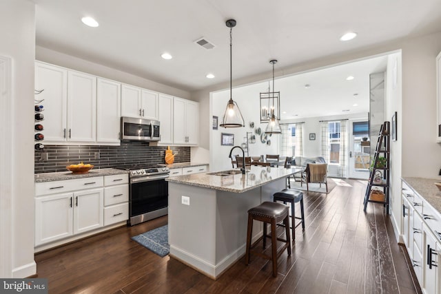 kitchen featuring appliances with stainless steel finishes, a sink, open floor plan, a kitchen bar, and visible vents