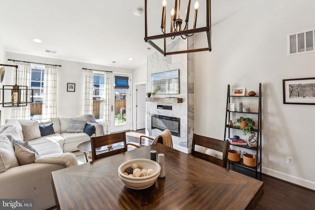dining room with an inviting chandelier, a premium fireplace, wood finished floors, and visible vents