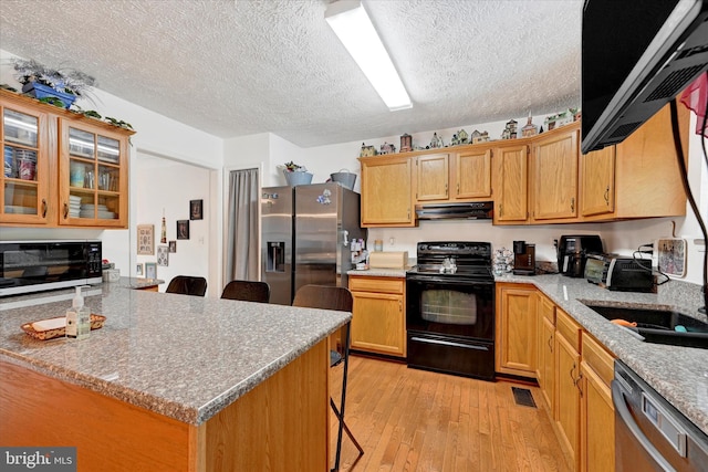 kitchen featuring a kitchen breakfast bar, a textured ceiling, appliances with stainless steel finishes, and light wood finished floors