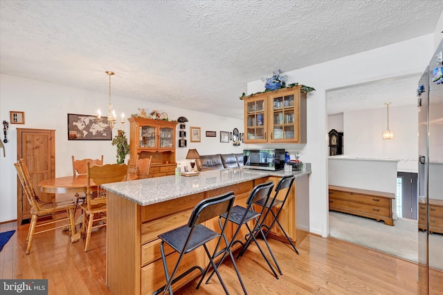 kitchen with light stone counters, light wood finished floors, a peninsula, stainless steel microwave, and glass insert cabinets