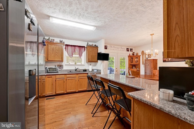 kitchen with a breakfast bar, french doors, light wood finished floors, and a textured ceiling