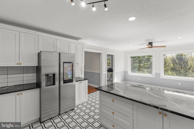 kitchen with a textured ceiling, ceiling fan, stainless steel refrigerator with ice dispenser, and white cabinetry
