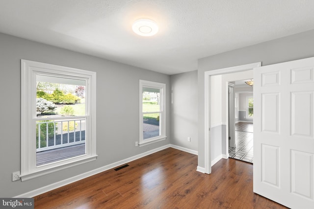 unfurnished room featuring baseboards, visible vents, dark wood-style floors, and a healthy amount of sunlight