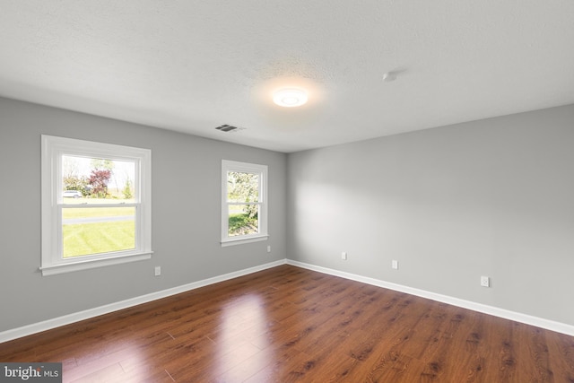 empty room with visible vents, dark wood-style floors, and a wealth of natural light