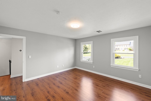 empty room with visible vents, a textured ceiling, baseboards, and wood finished floors