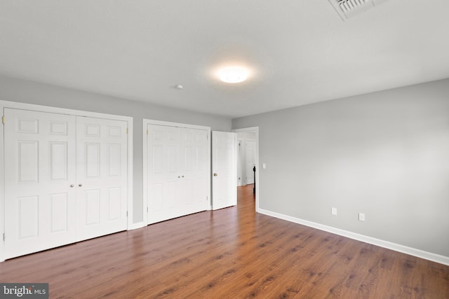 unfurnished bedroom featuring baseboards, two closets, wood finished floors, and visible vents