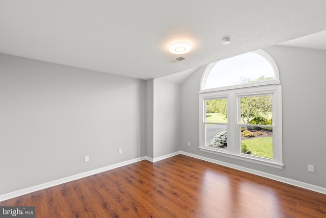 empty room featuring visible vents, baseboards, lofted ceiling, and wood finished floors