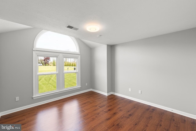 spare room featuring baseboards, visible vents, dark wood-style floors, and lofted ceiling