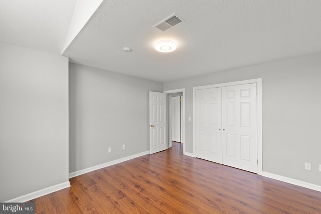 unfurnished bedroom with baseboards, wood finished floors, visible vents, and a closet