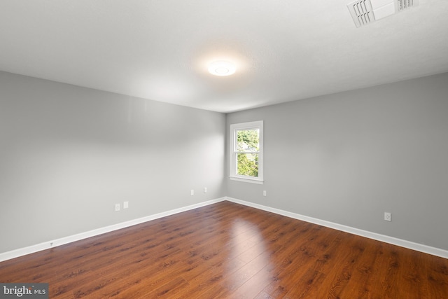 empty room featuring baseboards, dark wood-style floors, and visible vents