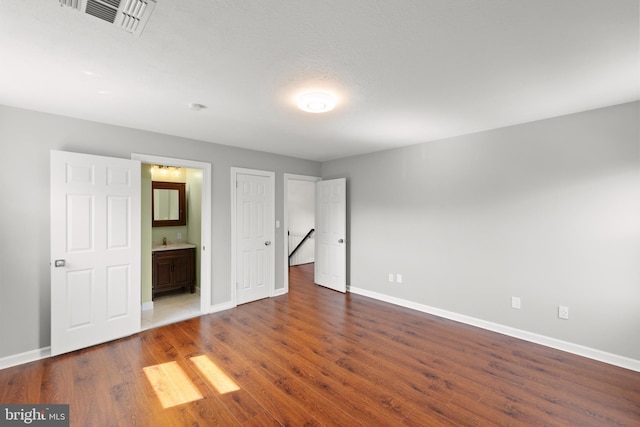 unfurnished bedroom featuring baseboards, visible vents, wood finished floors, and ensuite bathroom