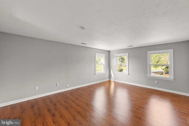 unfurnished room with baseboards, dark wood finished floors, a textured ceiling, and visible vents