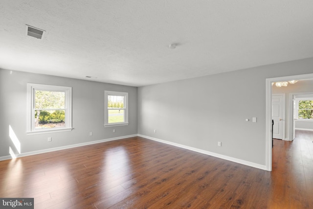 spare room with a textured ceiling, baseboards, visible vents, and dark wood-style floors