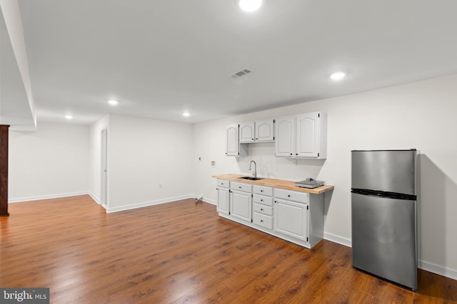 kitchen featuring visible vents, a sink, freestanding refrigerator, white cabinetry, and dark wood-type flooring