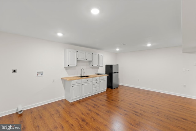 kitchen with a sink, freestanding refrigerator, white cabinetry, baseboards, and wood finished floors