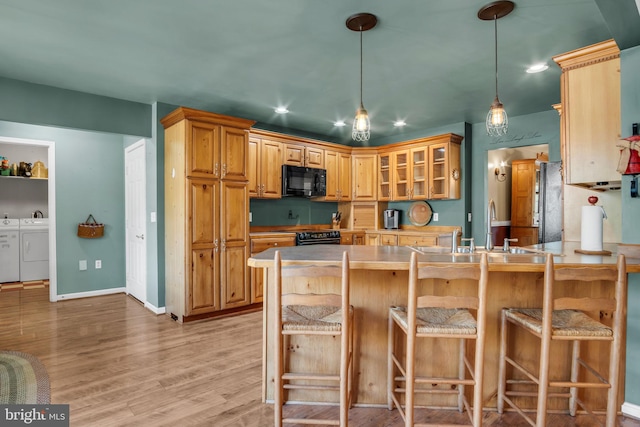 kitchen with black microwave, a sink, a peninsula, glass insert cabinets, and separate washer and dryer