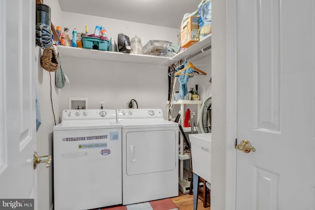 clothes washing area with laundry area, washing machine and dryer, a sink, and light wood-style flooring