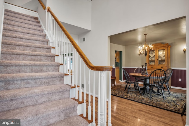 stairway featuring visible vents, wood finished floors, an inviting chandelier, and a wainscoted wall