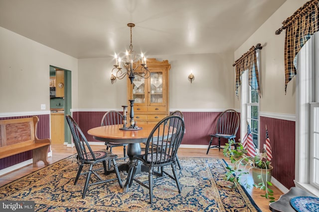 dining space with an inviting chandelier, wainscoting, and wood finished floors