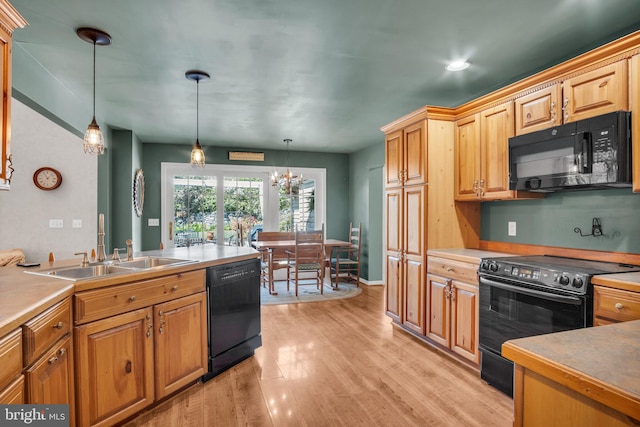 kitchen featuring hanging light fixtures, a sink, light wood finished floors, a chandelier, and black appliances