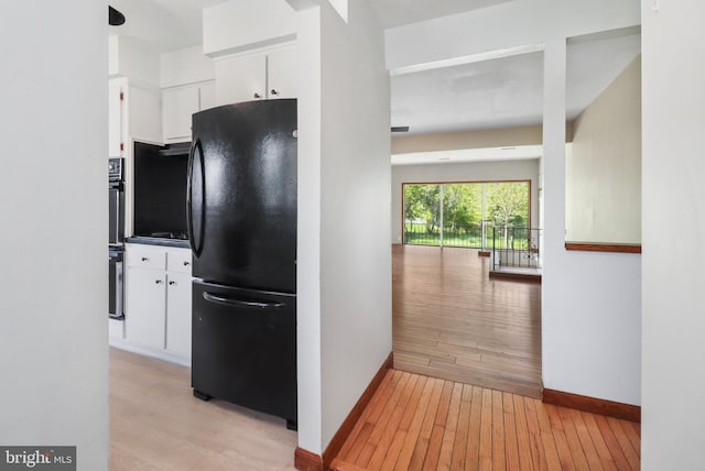 kitchen with light wood-style floors, freestanding refrigerator, baseboards, and white cabinets