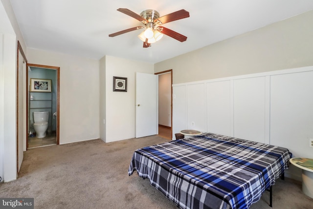 carpeted bedroom with a ceiling fan, a wainscoted wall, a closet, a decorative wall, and ensuite bath