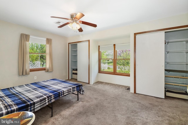 carpeted bedroom featuring ceiling fan, two closets, and visible vents
