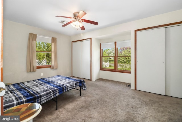 bedroom with two closets, ceiling fan, visible vents, and carpet floors