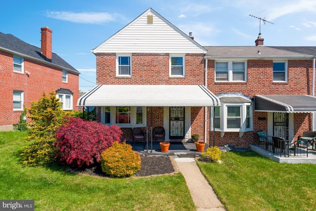 townhome / multi-family property with a porch, a front lawn, and brick siding