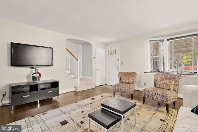living area featuring arched walkways, baseboards, stairs, and wood finished floors