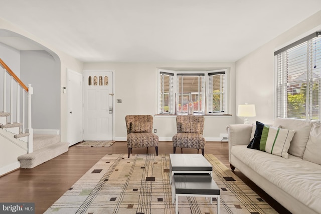 living room with baseboards, arched walkways, wood finished floors, and stairway