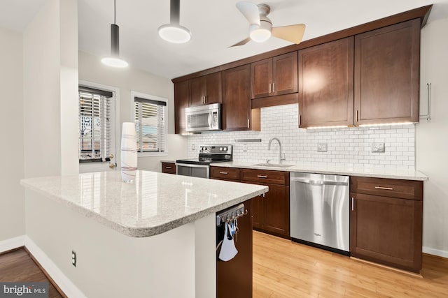 kitchen featuring backsplash, stainless steel appliances, a sink, and light wood-style flooring
